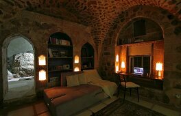 Beleuchteter Wohnbereich mit Tagesbett, in Nische eingerichteter Arbeitsplatz in historischem Wohnhaus, Gewölbe und Mauern aus Kalkstein
