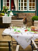 An embroidered tablecloth on a garden table with lots of wine glasses on a terrace