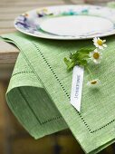 Name tag with chamomile flowers attached to green linen napkin