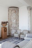Pale grey Rococo armchair next to stripped corner cupboard with rounded front