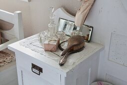 Hairbrush, hand mirror and various crystal bottles and jars on white-painted bedside cabinet