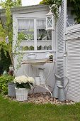 Vintage wash basin and pitcher on rusty metal stand and tub of white hydrangeas against outside wall of garden shed