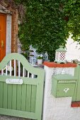 Green-painted wooden garden gate next to wall matching green post box mounted on garden wall