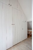 Cupboards with white-painted board fronts fitted on gable-end wall