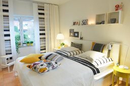 Vorhänge und Kissen mit grafischen Mustern in Grau und Gelb als freundliche Gestaltelemente in weißem Schlafzimmer