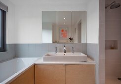 Zeitgenössisches Bad, Spiegelschrank über Waschtisch mit Unterschrank aus Holz und eingebaute Badewanne am Fenster