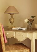Rattan chair at delicate, carved console table with vintage table lamp with old rose lampshade
