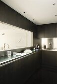 Designer kitchen with dark fronts, stainless steel splashback and hatch above narrow counter with view of modern artwork in dining area