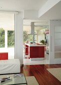 Blick vom Wohnraum mit Edelholzparkett durch die offene Schiebetür auf einen zentralen Küchenblock mit roten Fronten