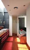 Schmales Designerbad mit seitlichem Lichtschacht über Doppelwaschtisch und eingebauter Wanne mit Holzverkleidung