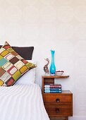 Retro-patterned scatter cushion on bed next to wooden bedside cabinet