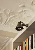 Antique-style wall lamp attached to bookcase in interior with floral, stucco ceiling