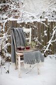 Tablett mit Glühwein und Decke auf altem Holzstuhl in schneebedecktem Garten