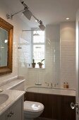 Modern, white-tiled bathroom with traditional ambiance; bathtub with rainfall shower behind glass screen, Tolomeo wall lamps and gilt-framed mirror