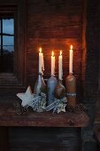 Rustikaler Adventskranz mit vier brennenden Kerzen in verschiedenen Flaschen aus Steingut