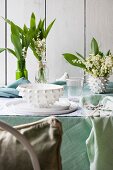 White place setting, lily of the valley and pastel green tablecloth on table outdoors