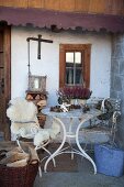 White vintage garden table and sheepskins on garden chairs outside farmhouse; potted heather and pine cones on table