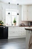 White fitted kitchen and black pendant lamps in front of window
