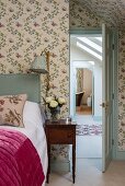 Romantic bedroom with floral wallpaper, antique bedside table and view through open door