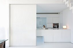 Wide doorway with white sliding door leading into white, modern fitted kitchen