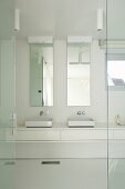 Open glass door and view of modern, white washstand with twin sinks below tall narrow mirrors