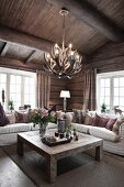 Solid wooden coffee table and pale sofa set under light fitting made from antlers in living area of wooden house