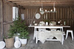 White table and bench with white sheepskins next to small potted Christmas trees in wooden house