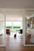 Arbeitszimmer mit Möbelklassikern und Gartenblick, im Vordergrund Glastrennwand mit weiss lackiertem Holzrahmen
