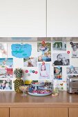 Collection of photos on magnetic pinboard between wooden kitchen base cabinets and white wall cabinets