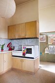 Simple retro kitchen area with electronic appliances on base units and pale wooden wall units