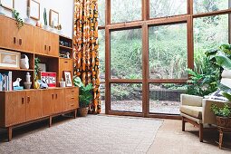Retro living room cupboards next to glass wall with view of garden