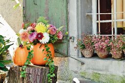 Bouquet in hollowed-out pumpkin used as vase on tree stump outside rustic house