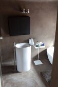 Weißes Standwaschbecken mit Standarmatur in reduziertem Designerbad mit schwarzem Hängeschränkchen und Betonboden