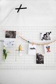 Photos and bead necklace hung on white metal mesh used as pinboard and minimalist pendant lamp stuck on wall with black tape