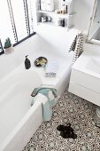 White bathroom with Moroccan-style ornamental floor tiles and wall-mounted shelves above bathtub