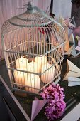 Ehemaliger Vogelkäfig mit brennenden Stumpenkerzen, davor pinkfarbene Hortensienblüten