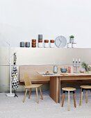 Modern dining table, wooden chair, stools and bench against half-height wall panel with elegant crockery on top