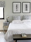 Double bed with white bed linen and black and white patterned pillows; vintage bedside cabinet and black-framed pictures against pale grey wall