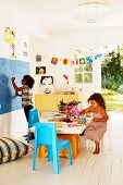 Children playing on table and drawing on chalkboard in decorated children's bedroom with open door leading to garden