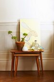 Two-piece set of wooden side tables, arrangement of potted plant and picture of hare against white wainscoting