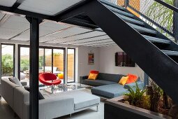 Eleganter Loungebereich mit Ecksofas vor Terrassentür, im Vordergrund Stahltreppe