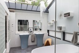 Elegant designer bathroom in subtle shades with twin pedestal sinks and glass ceiling