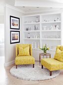 Yellow easy chairs and side table on round rug in front of white ornaments on white shelving
