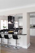 Open-plan, American-style kitchen with black worksurface and breakfast bar with bar stools