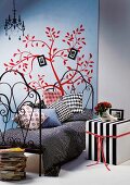 Black and white striped cubic side table next to metal bed against poster of red, stylised tree on wall