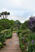 Narrow stone-paved path leading to fountain in flowering garden