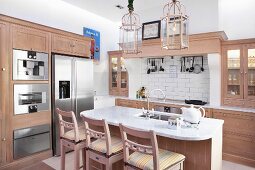 Breakfast bar and bar stools in open-plan kitchen with pale wooden cabinet in modern, country-house style
