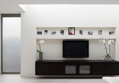 Low, black sideboard and flatscreen TV in niche in contemporary living room
