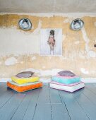 Colourful stacked floor cushions in front of retro wall-mounted lamps and picture on patinated wall