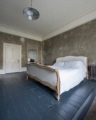 Sleigh bed on slate grey wooden floor in bedroom with patinated walls